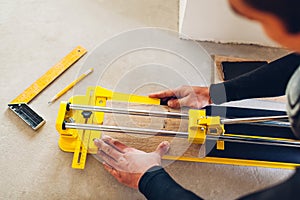 Construction worker using manual cutter equipment for laying processing ceramic tiles on floor. Professional tool