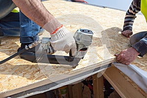 Construction worker using nail gun to nail Oriented Strand Board osb sheeting on roof of a new home.