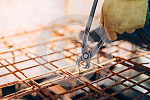 Construction worker using pliers and securing steel bars with wire rod for reinforcement of concrete or cement