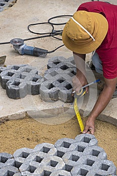 Construction worker using tape measure to measuring gaps in walkway for cut turf stone block in paving pavement work