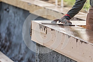 Construction Worker Using Wood Trowel On Wet Cement Forming Coping Around New Pool