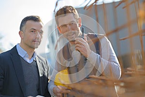 construction worker on walkie talkie behind stack rebars