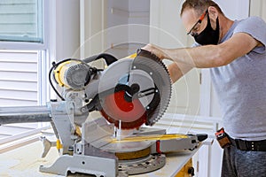 Construction worker wearing a medical mask to prevent Covid-19 is works on remodeling home carpenter cutting wood molding on with