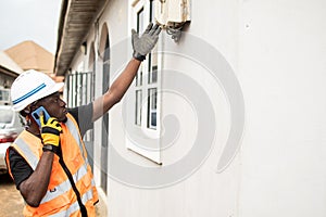 a construction worker wearing an orange vest and white hat, pointing at a brick wall