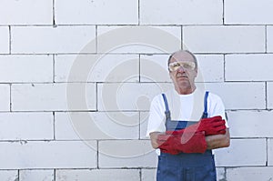 Construction worker wearing prfessional overalls and red protective gloves, standing near the white bricks wall