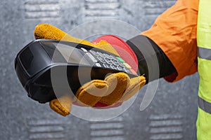 Construction worker wearing protective gloves and reflective workwear holding a wireless payment terminal. Concept of digital