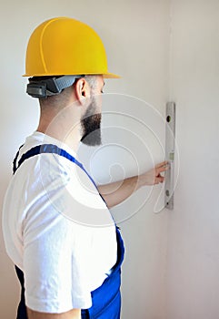 Construction worker is working on renovation of apartment. Builder is measuring and checking wall room using spirit level tool.