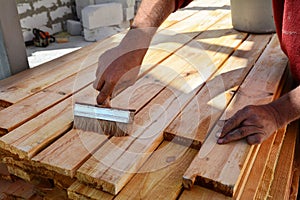 Construction worker is working with wooden beam. The worker brushes the preservative liquid on the folded boards and boards.