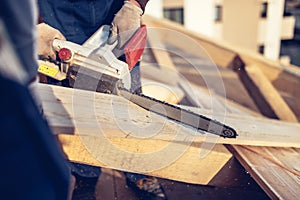 Construction workers cutting timber wood with chainsaw. Men sawing using electrical chainsaw at roof construction