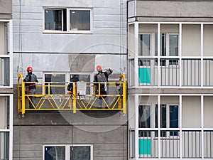 Construction workers installers high-rise workers industrial climbers, painters on the lift paint the facade of the building, comp