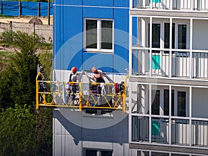 Construction workers installers high-rise workers industrial climbers, painters on the lift paint the facade of the building, comp