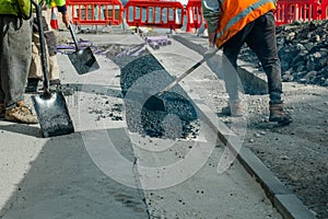 Construction workers placing hot tarmac after installation of new underground services, kerbs