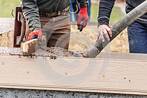 Two Construction Workers Pouring And Leveling Wet Cement Into Wood Framing