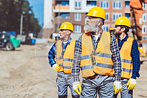 Construction workers in reflective vests and hardhats standing outside, examining the