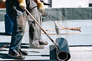 Construction workers, roofers installing rolls of bituminous waterproofing membrane for the waterproofing of new house. House