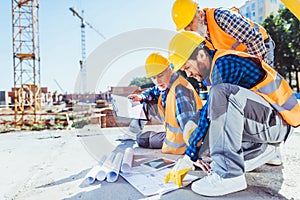 construction workers in uniform sitting on concrete at construction site, discussing