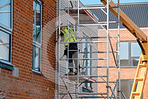 Construction workers using aluminium mobile scaffold tower and safety harness to work at height.