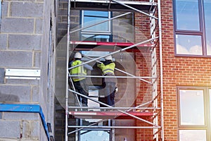 Construction workers using aluminium mobile scaffold tower and safety harness to work at height. Working at height safety