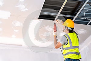Construction workers using an electric drill are install the ceiling house in the building under construction, Ceiling