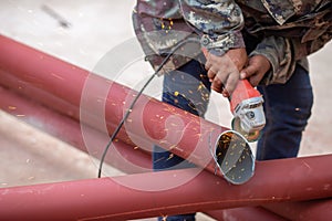 Construction workers are using grinding machines on large steel pipes. Used as a roof pole. Sparking while working Red painted