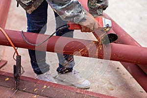 Construction workers are using grinding machines on large steel pipes. Used as a roof pole. Sparking while working Red painted