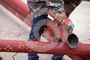 Construction workers are using grinding machines on large steel pipes. Used as a roof pole. Sparking while working Red painted