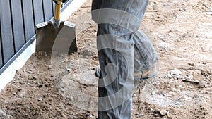 Construction working man uses a flat shovel to scrape brown dirt by a wall.