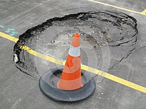 Constructions at unexpected sink hole in public parking lot with traffic cone