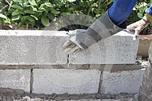 Constructor hand wear rubber gloves holding a concrete block to build a fence.