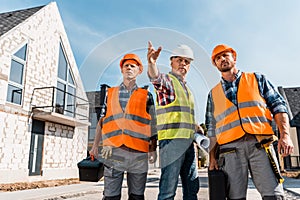 Constructors in helmets holding toolboxes near coworker gesturing