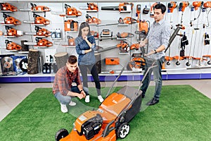 A consultant in a garden tools store shows a guy and a girl a lawn mower.