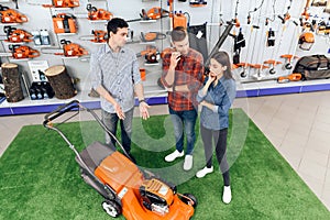 A consultant in a garden tools store shows a guy and a girl a lawn mower.