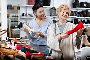 Consultant in shoeshop helping old woman to choose footwear