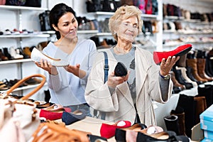 Consultant in shoeshop helping old woman to choose footwear