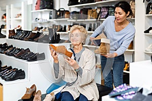 Consultant in shoeshop helping old woman to choose footwear