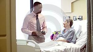 Consultant Talks To Senior Female Patient In Hospital Room