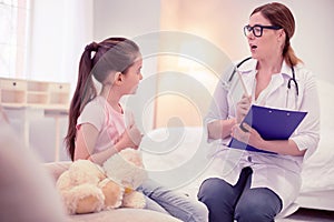 Pleasant dark-haired family physician consulting cute little girl photo