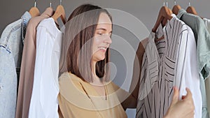 Consumer fashion. Retail store. Vogue clothing. Stylish garments. Joyful young adult woman standing near hangers with clothes