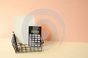 Consumer shopping basket with calculator, pencil, memo pad on ivory and pink background. Economic Concept