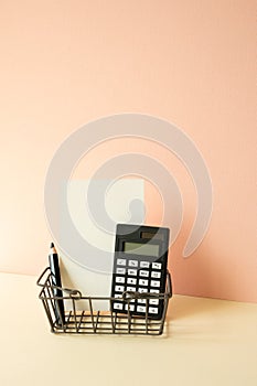 Consumer shopping basket with calculator, pencil, memo pad on ivory and pink background. Economic Concept