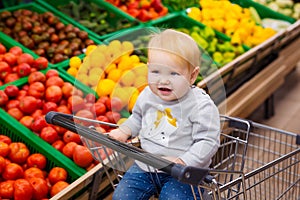 Consumerism concept. Baby in cart doing grocery shopping at supermarket