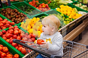 Consumerism concept. Baby in cart doing grocery shopping at supermarket