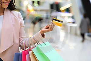 Consumerism Concept. Black woman with shopping bags and bank card in mall