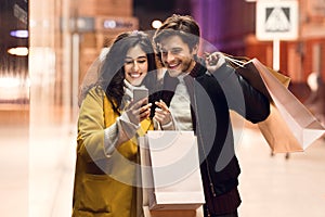 Consumerism concept. Couple with paper bags and smartphone