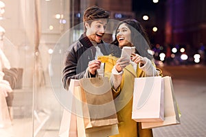 Consumerism concept. Happy couple checking cellphone outdoors