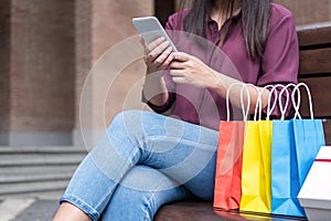 Consumerism, shopping, lifestyle concept, Young woman sitting near shopping bags and gift box while playing smartphone enjoying in