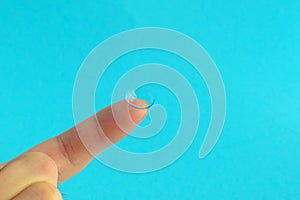 Contact lens on finger on lblue background.