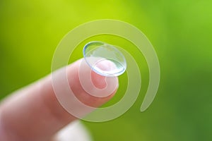 Contact lens on finger tip on blurred green summer nature background