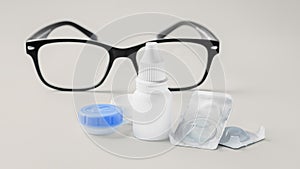 Contact lens, solution and container with eyeglasses on beige background