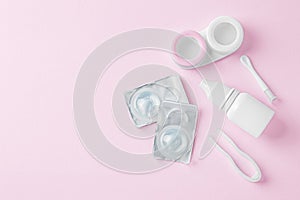 Contact lenses with container, eye drop and tweezer on pink background, top view